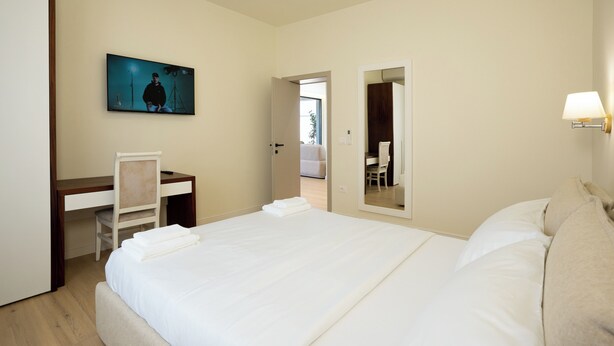 A hotel room with a bed, a desk, a chair, a TV, and a mirror. - Villa Cosmo (Rrashbull)