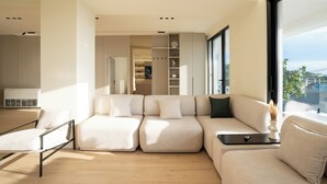 A modern living room with a sectional sofa, a small table with a vase, and a view of the outdoors through large windows. - Villa Cosmo (Rrashbull)