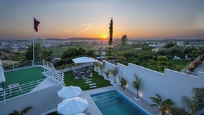 A rooftop pool area with a view of the sunset, a flag, and a landscaped garden. - Villa Cosmo (Rrashbull)