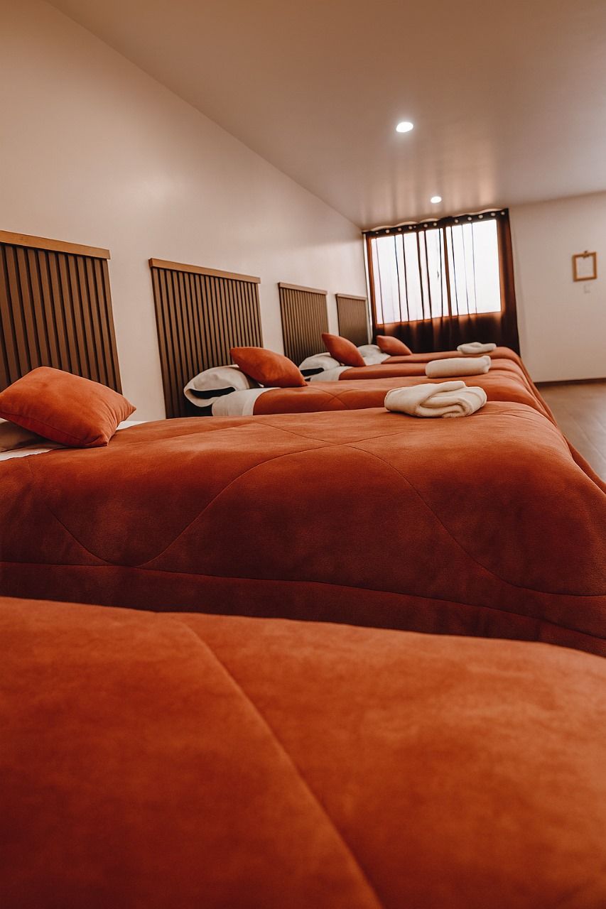 A hotel room with three beds, each with orange bedding and white pillows.