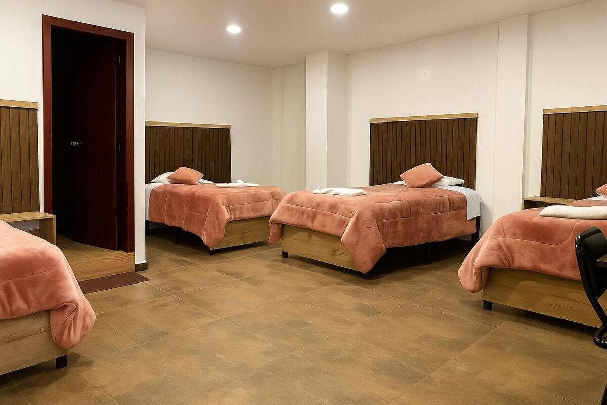 A hotel room with four beds arranged in a row, each with a wooden headboard and pink bedding.