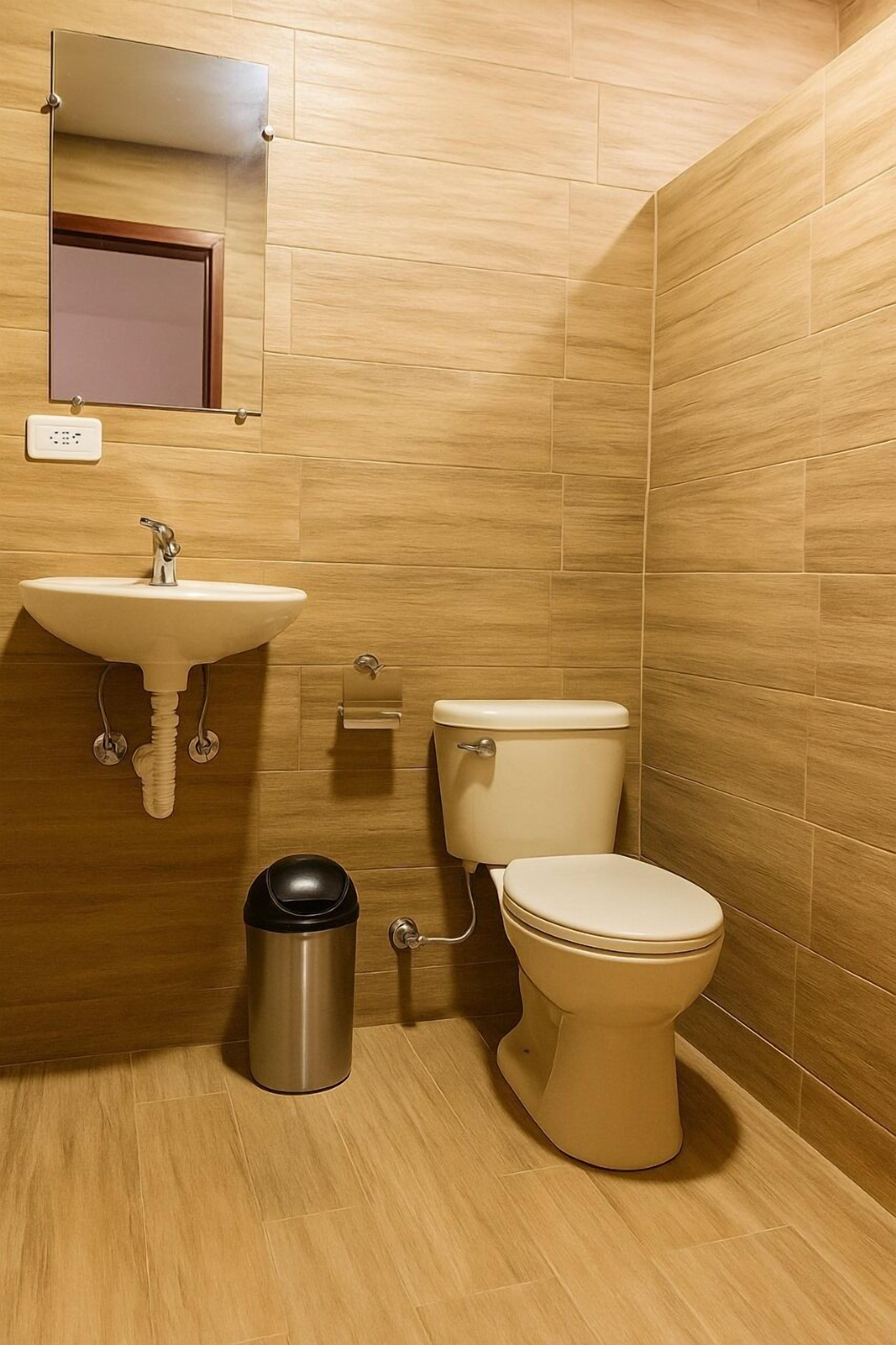Un baño con lavamanos, inodoro y cubo de basura.