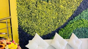 A room with a white sofa, a glass table with food, and a wall with green foliage. - HOSTERIA DON POLY (San Miguel de Salcedo)