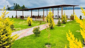 A gazebo with a tiled roof and wooden pillars, surrounded by a grassy area with small trees and a paved path. - HOSTERIA DON POLY (San Miguel de Salcedo)
