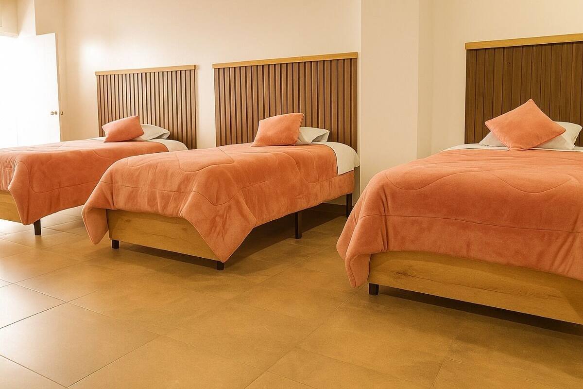 Three single beds with wooden headboards in a room with tiled flooring.