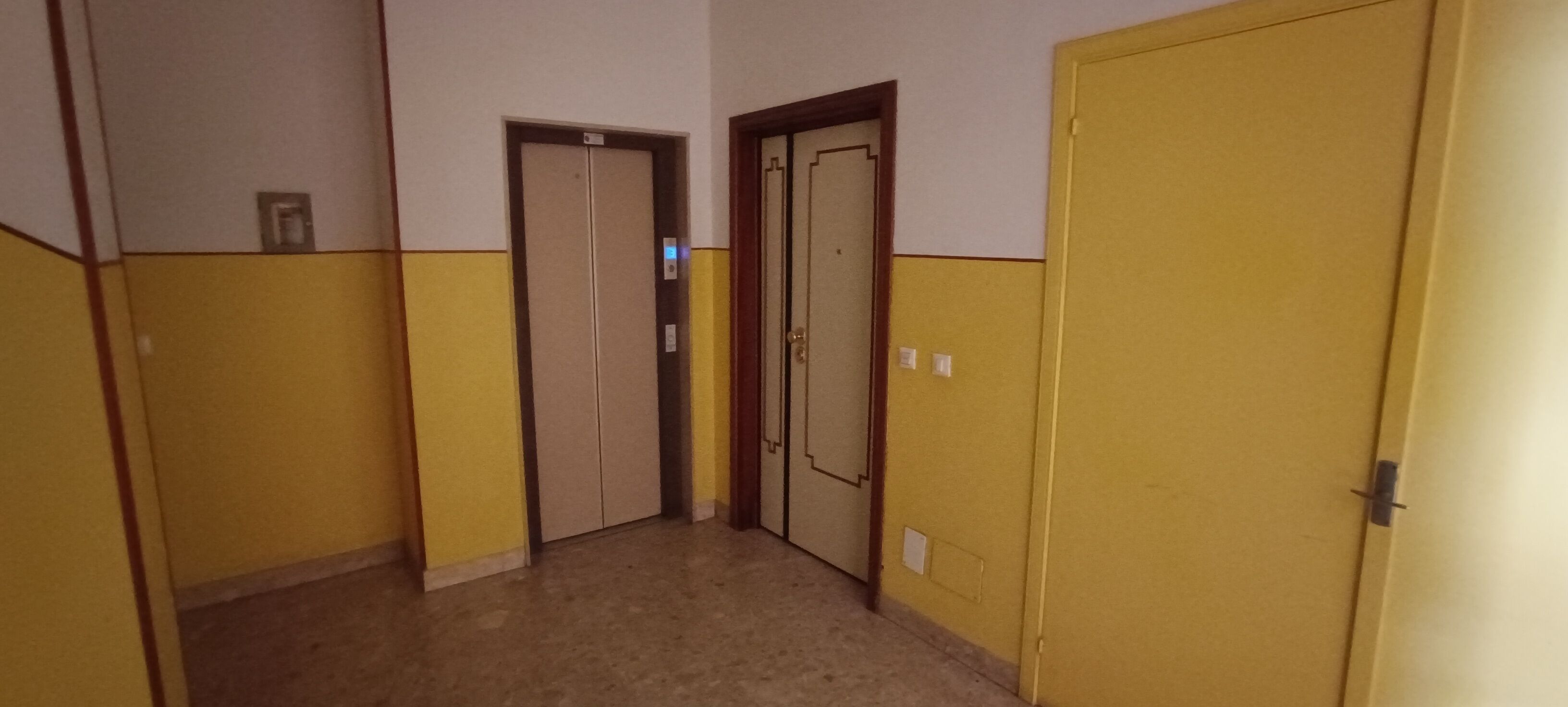 Un corridoio con due porte, una con l'interruttore della luce e l'altra con una maniglia.