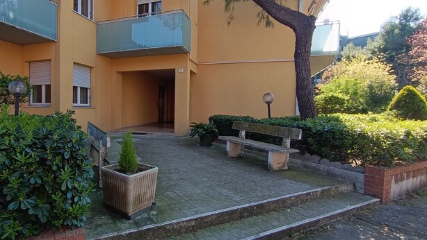 A residential building with a paved courtyard, a bench, and a potted plant.