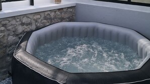 Un bain à remous dans une pièce aux murs de pierre, avec une fenêtre donnant sur un paysage verdoyant.