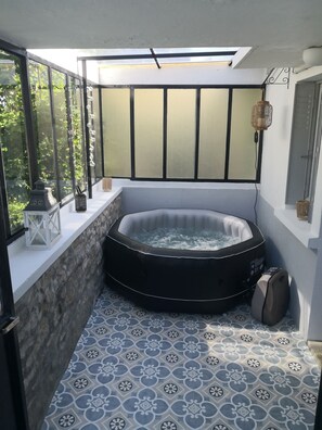 A hot tub in a corner with a stone wall and a window. - Small atypical country house. (Saint-Martin-le-Mault)