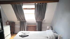 Une chambre à coucher avec un lit, une commode et une fenêtre avec des rideaux.