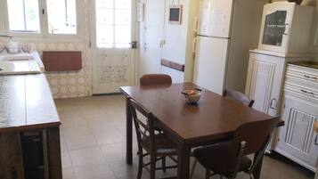 A kitchen with a wooden table and chairs, a refrigerator, and a window with a view of the outside.