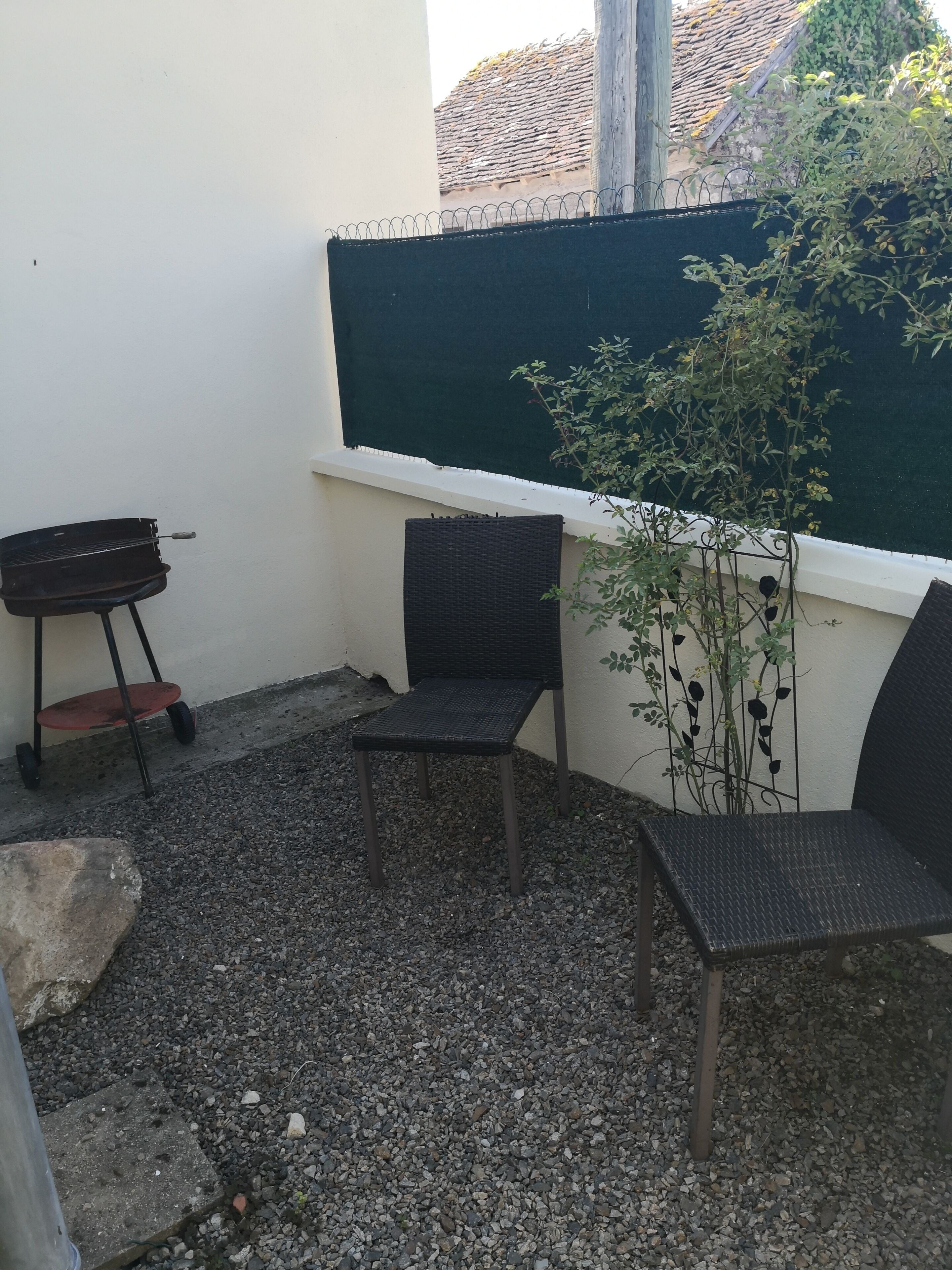 Eine Terrasse mit zwei Korbstühlen, einem kleinen Grill und einem Blumentopf.