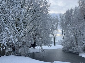 Paisaje nevado con río, árboles y una estructura de madera.