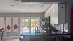 Une cuisine moderne avec un îlot central, des tabourets de bar et une vue sur une clôture rouge, visible à travers la porte.