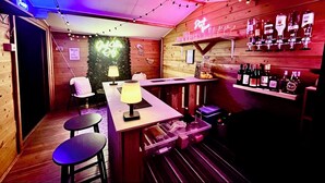 A bar area with wooden walls, a neon sign, and shelves of bottles.