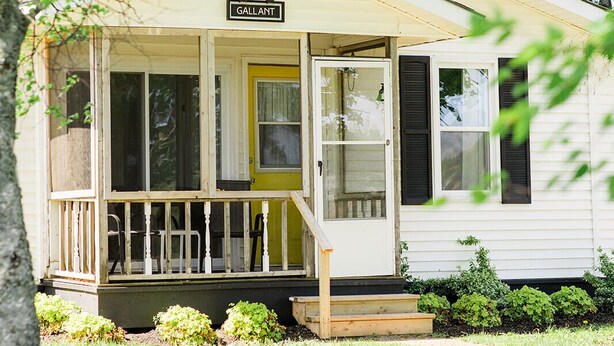 A small, single-story house with a porch, a yellow door, and a sign that reads "GALLANT." - Gallant Cottage-PEI Charm, updated cottage with AC near Charlottetown. Waterview (Alexandra)