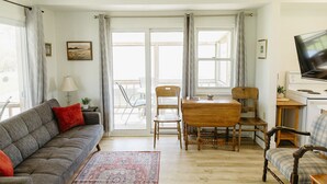 A living room with a sofa, a dining table with chairs, a television, and a view through the glass doors. - Gallant Cottage-PEI Charm, updated cottage with AC near Charlottetown. Waterview (Alexandra)