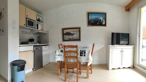 A compact kitchen with a microwave, sink, and cabinets, a dining table with chairs, and a TV on a cabinet.