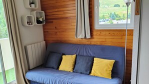 A cozy room with a blue sofa, a black rug, wooden paneling, a window with a view, and a radiator.