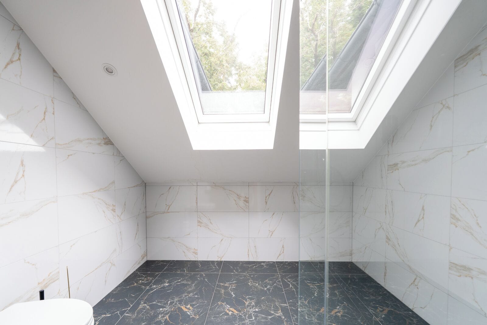 Un baño moderno con paredes de mármol blanco, suelo de mármol negro y tragaluces.