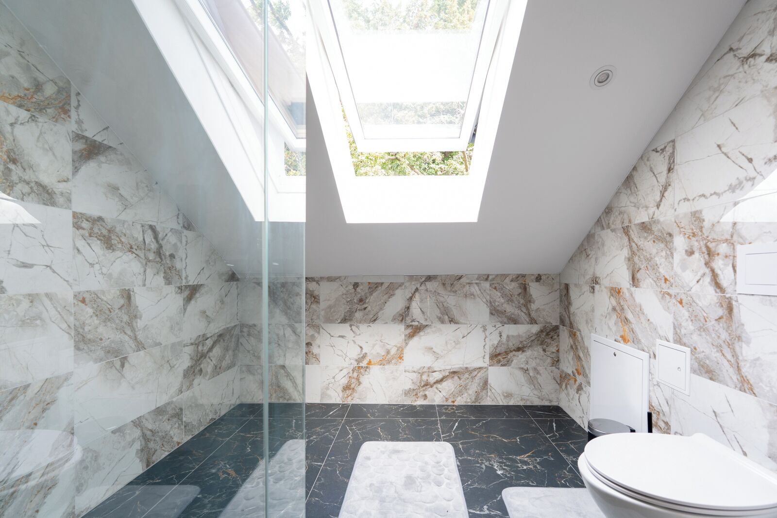 Een moderne badkamer met een dakraam, marmeren wanden en een zwarte marmeren vloer.