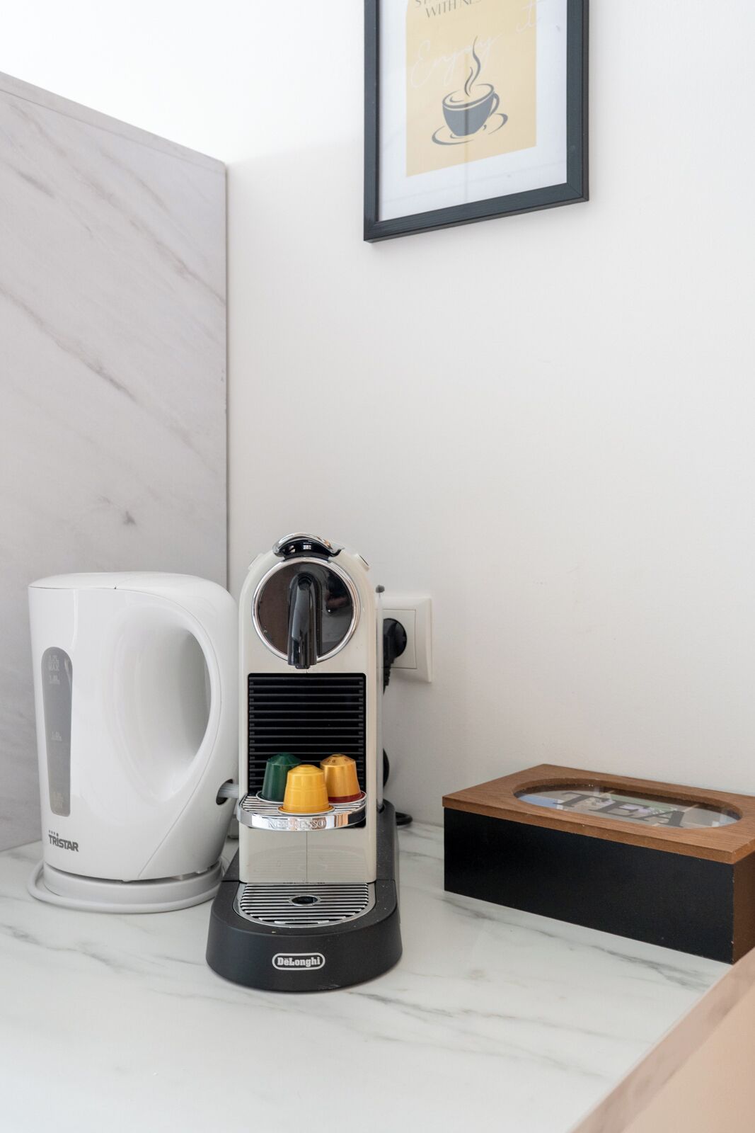 Eine Kaffeemaschine, ein Wasserkocher und ein gerahmtes Bild auf einer Marmorarbeitsplatte.