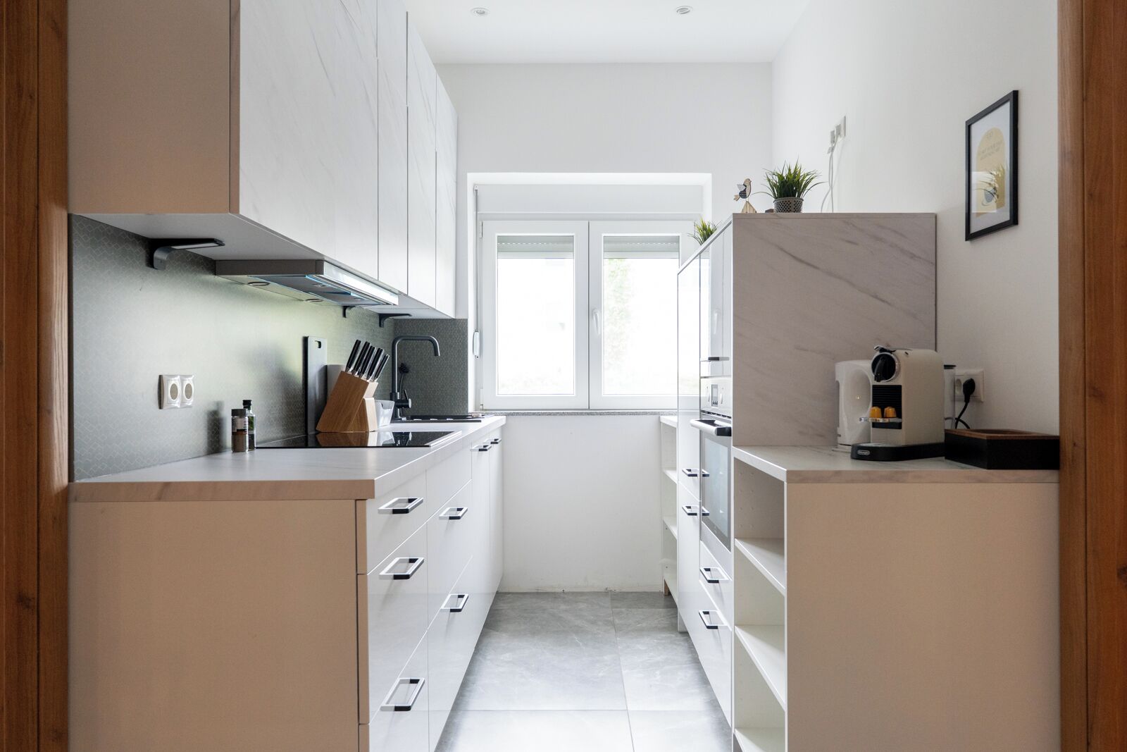A modern kitchen with white cabinetry, a built-in oven, and a coffee machine.