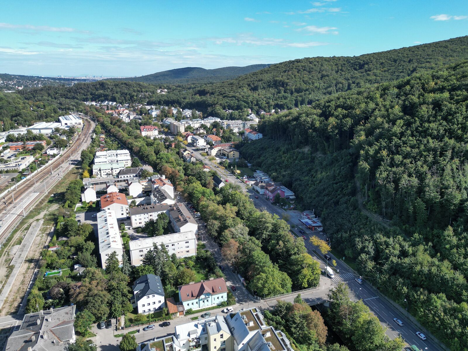 An aerial view of a town with a mix of residential and commercial buildings, surrounded by dense forest.