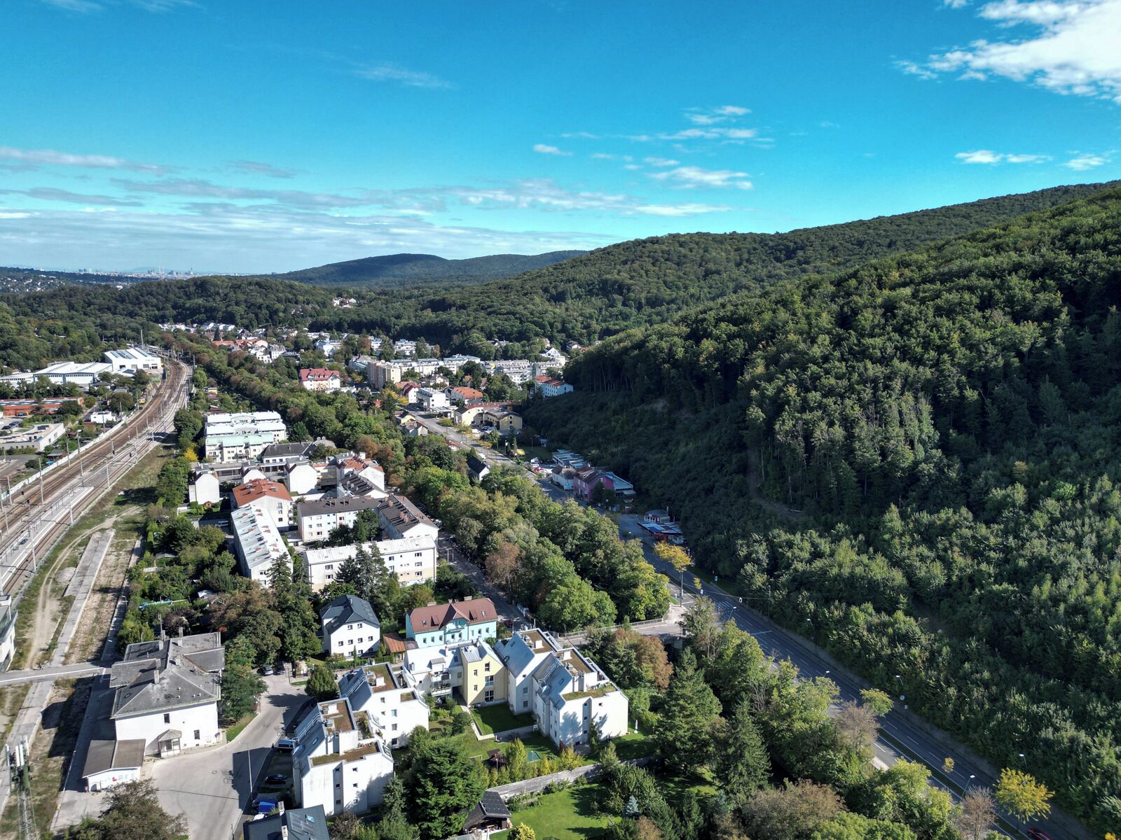 Ett flygbildsbild av en stad med en blandning av bostads- och kommersiella byggnader, omgiven av täta skogar och kullar.