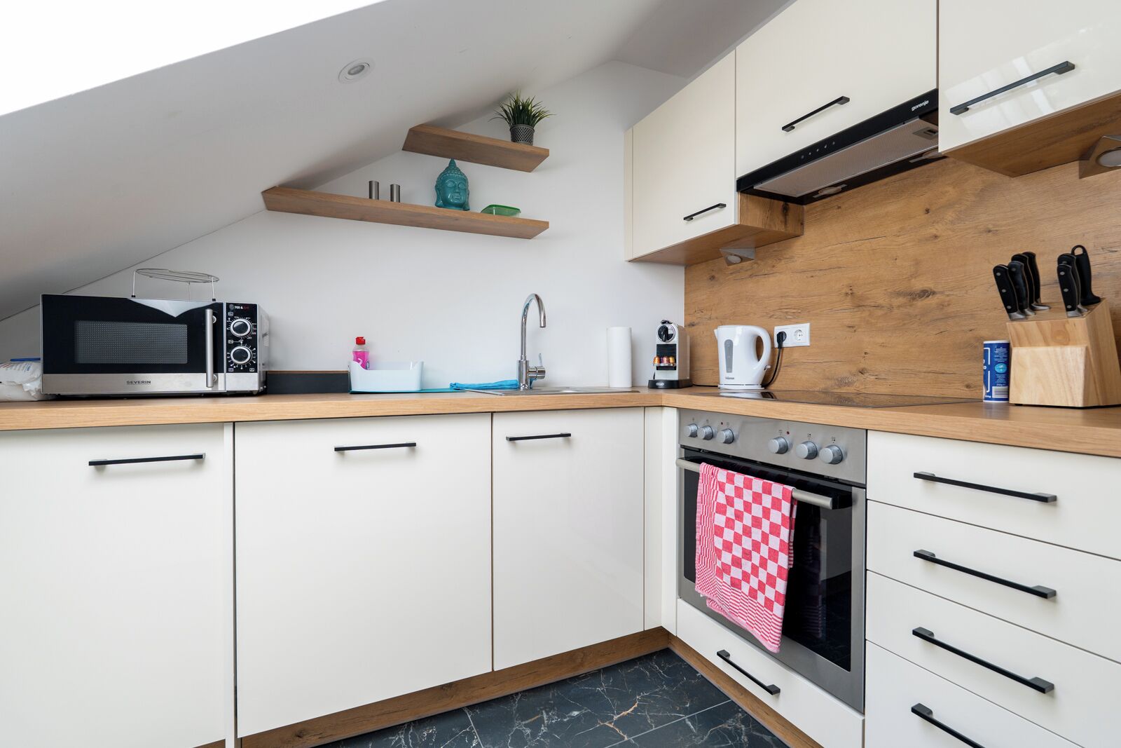 Een moderne keuken met witte kastjes, een houten aanrecht, een magnetron, een oven en een spoelbak.