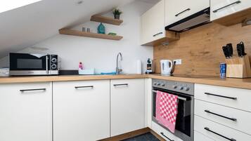 Een moderne keuken met witte kastjes, een houten aanrecht, een magnetron, een oven en een spoelbak.