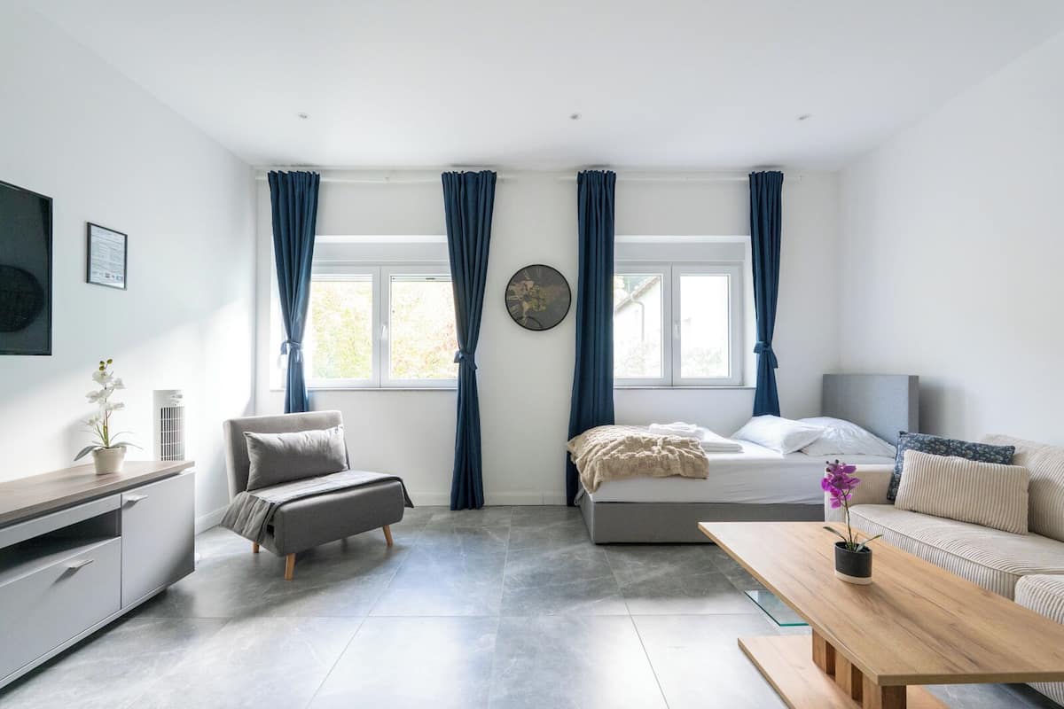 Ein modernes, helles Zimmer mit einem Bett, einem Sofa, einem kleinen Tisch und einem Schreibtisch.