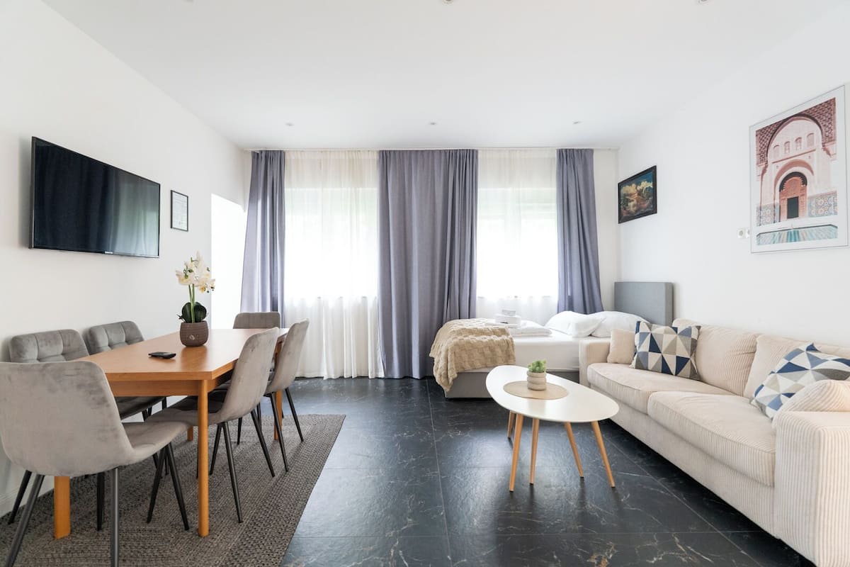 Ein modernes Wohnzimmer mit Essbereich, einer Couch, einem Couchtisch und einem an der Wand befestigten Fernseher.