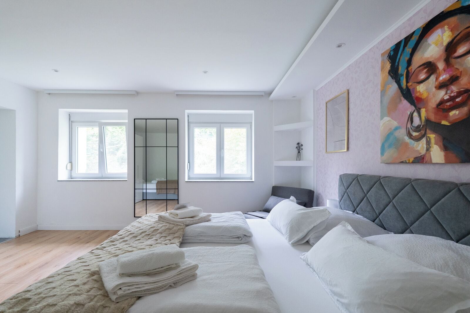 Een moderne slaapkamer met een groot bed, een grijs gestoffeerd hoofdbord en een groot raam.