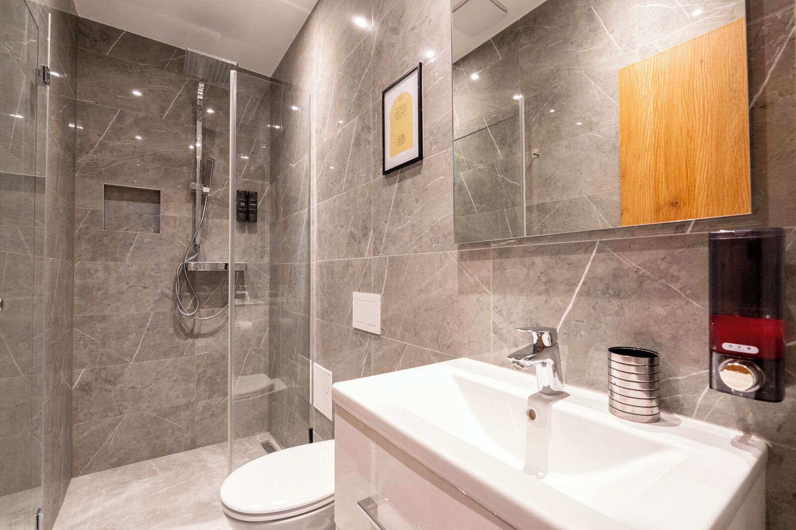 Une salle de bain moderne avec une douche à parois de verre, un lavabo blanc doté d’un robinet chromé et un meuble-lavabo en bois.