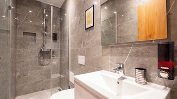 Une salle de bain moderne avec une douche à parois de verre, un lavabo blanc doté d’un robinet chromé et un meuble-lavabo en bois.