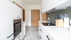 Een moderne keuken met witte kasten, een ingebouwde oven, een houten deur en een aanrecht met een messenblok en een snijplank.