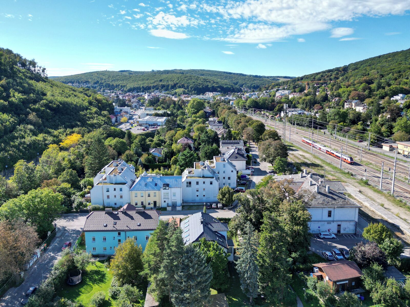 Un quartier résidentiel avec des maisons, une ligne de chemin de fer et un paysage vallonné.