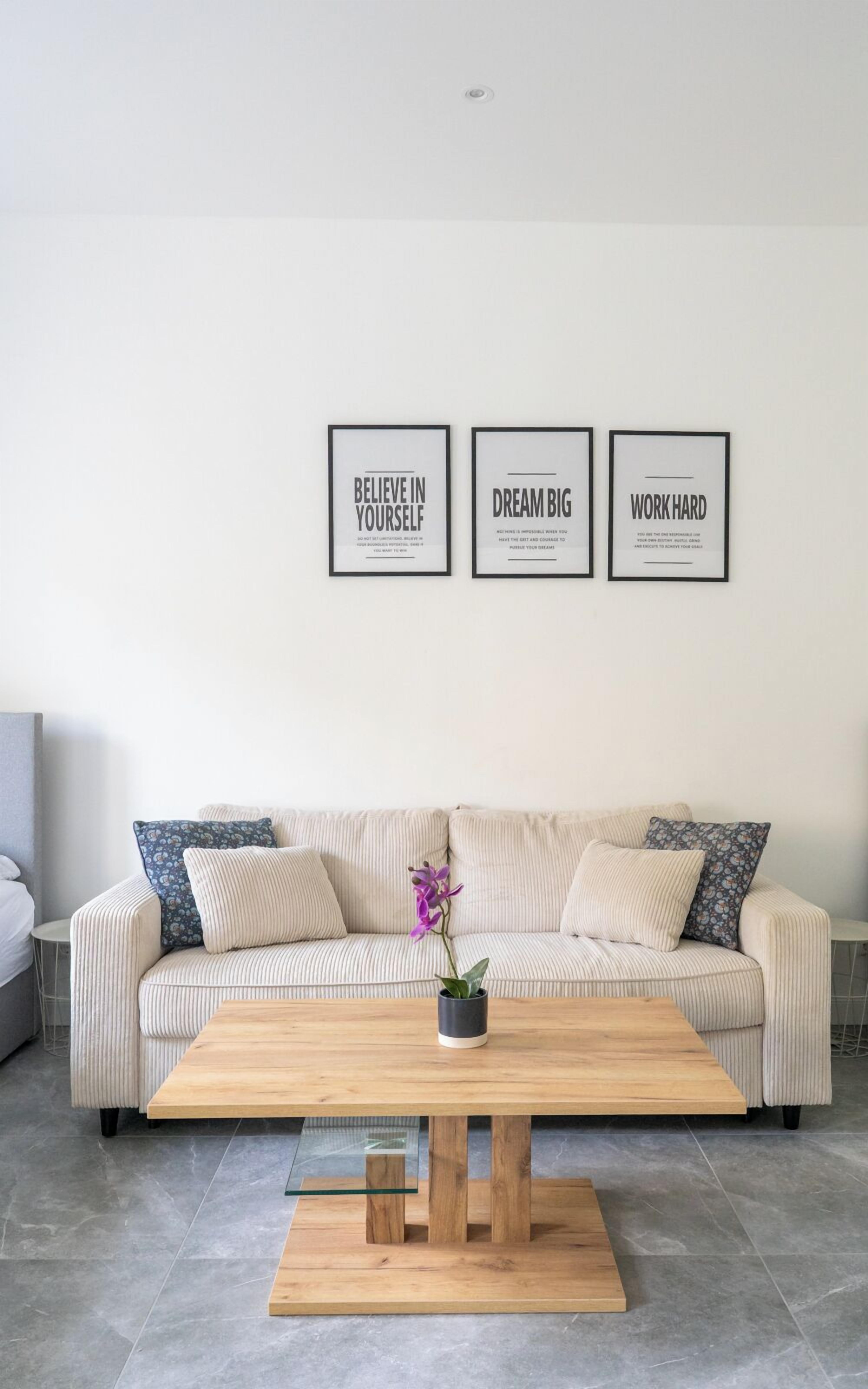 A modern living room with a beige sofa, a wooden coffee table, and three motivational posters on the wall.