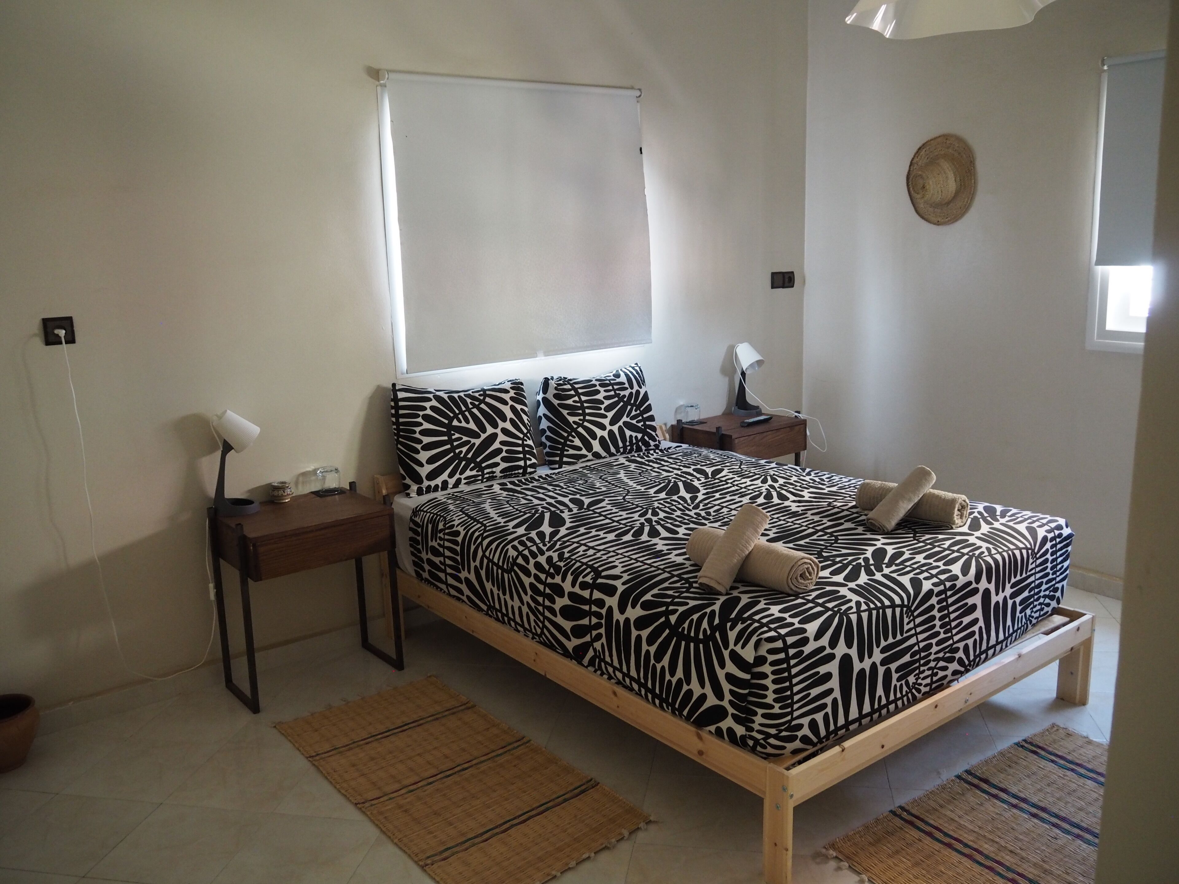 A bedroom with a bed, bedside tables, a lamp, a window, and a wall-mounted hat.