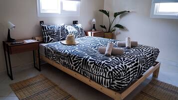 A bedroom with a bed, nightstands, a lamp, a plant, and a window.