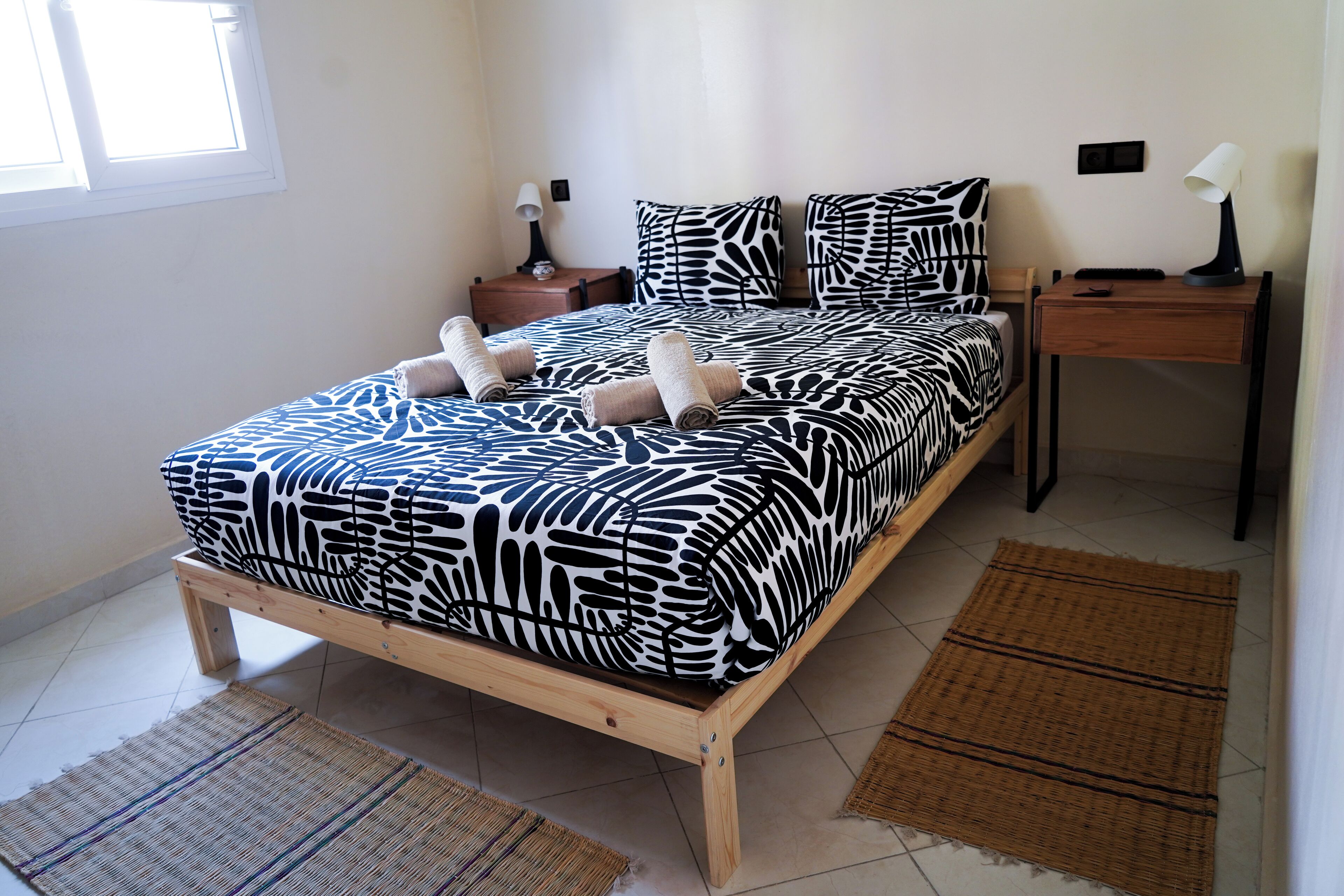 Un lit recouvert d’une couvre-lit à motifs zébrés, deux tables de chevet avec des lampes et une fenêtre avec des stores.