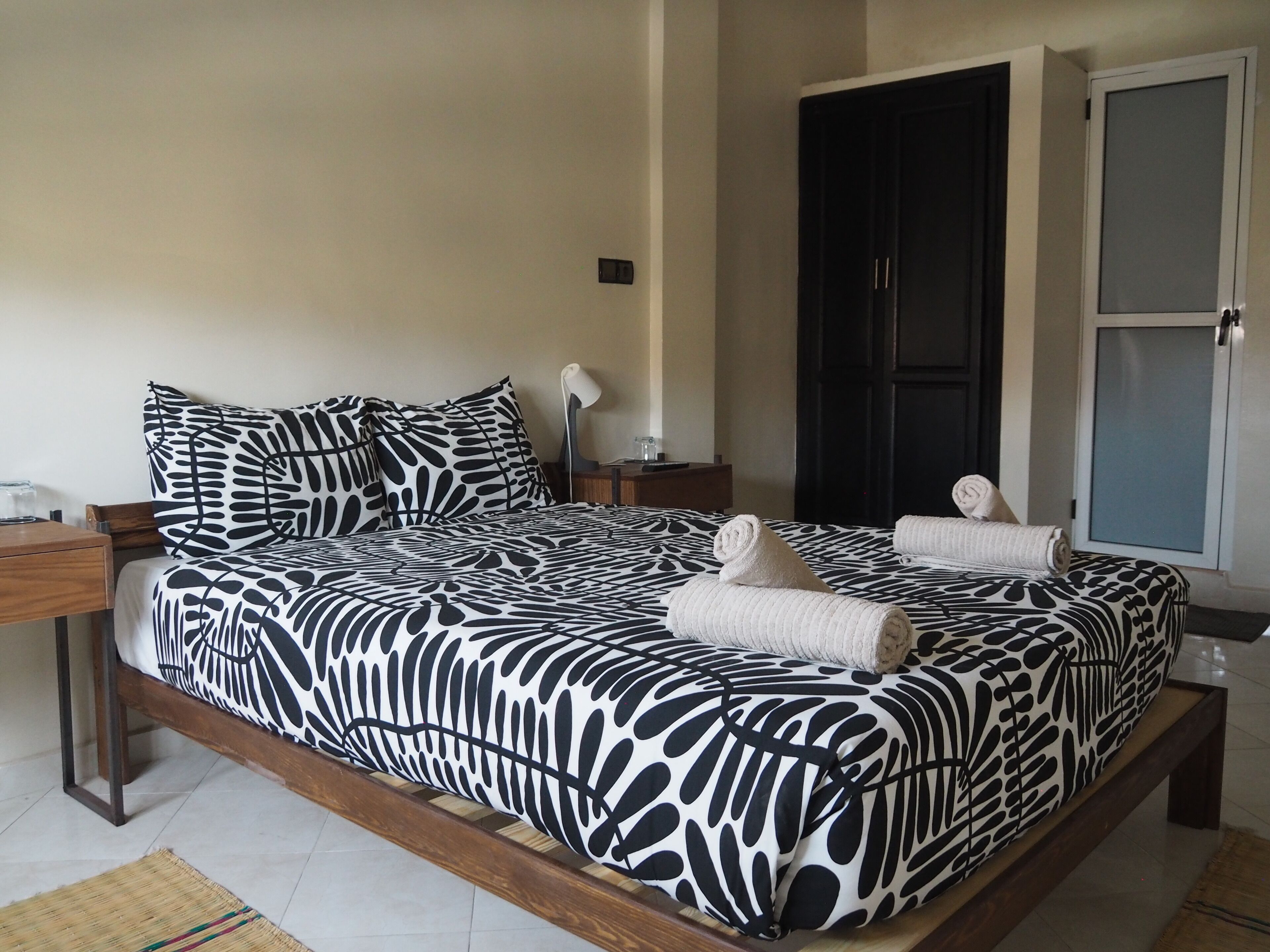 A bedroom with a zebra-patterned bedspread, a wooden headboard, a bedside table with a lamp, and a door with a frosted glass panel.