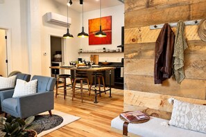 Un salon moderne avec un canapé, un coin repas comprenant une table et des chaises, et une cuisine agrémentée d’éléments en bois.