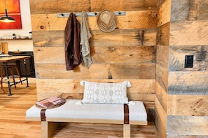 Un coin salon accueillant avec un banc, une étagère fixée au mur sur laquelle sont posés un chapeau et une veste, et un mur en bois orné d’un motif texturé.