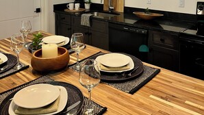 A modern kitchen with black countertops, wooden dining table, and pendant lights.