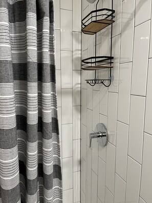 A bathroom with white tiled walls, a striped shower curtain, and a metal shower tray with a faucet.