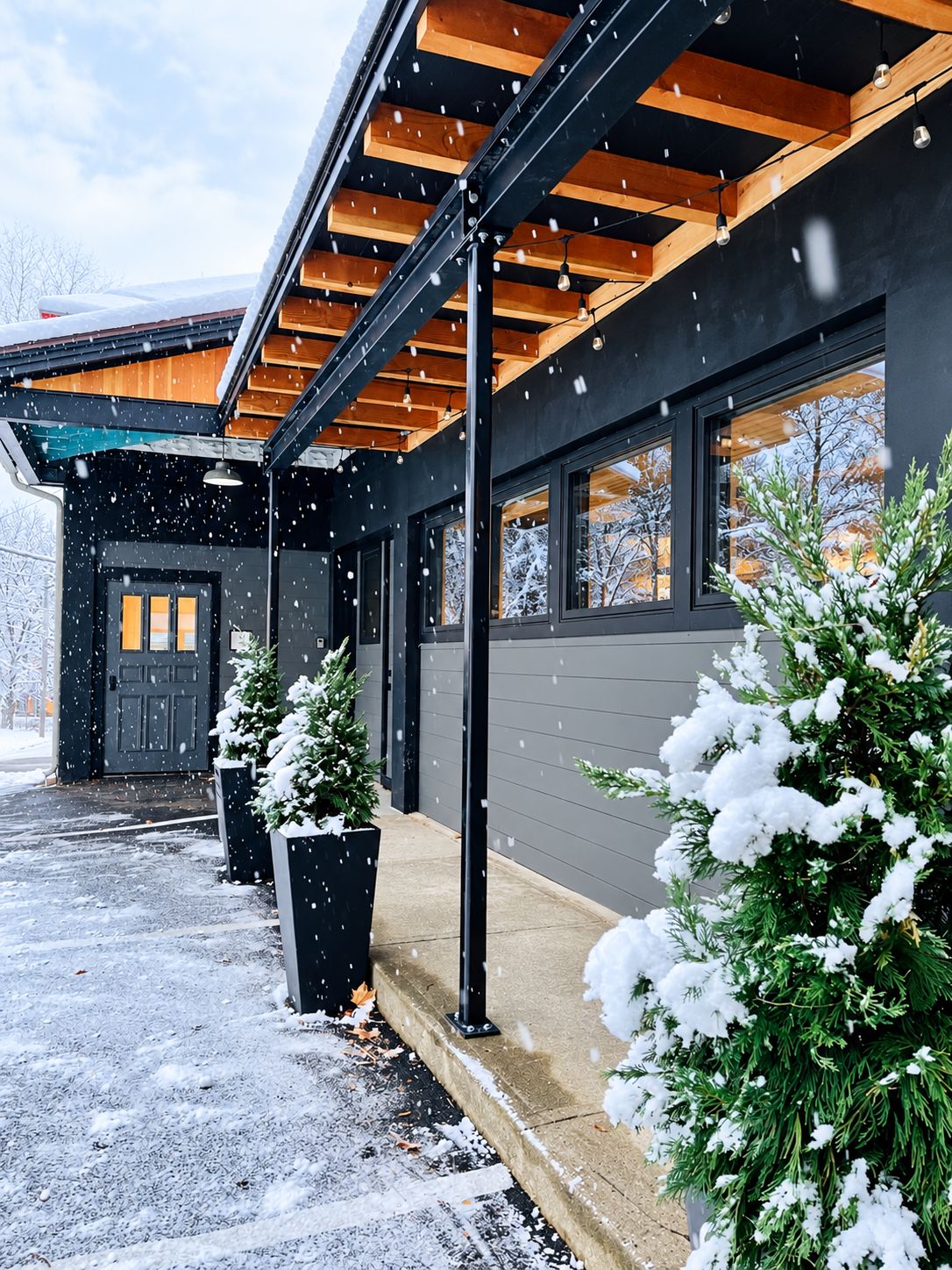 Un bâtiment moderne doté d’un porche abrité, de grandes fenêtres et de plantes recouvertes de neige.