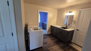 A compact kitchen with dark wood flooring, a built-in sink, and a white washing machine. - Just Like Home, brand new 2 bedroom rancher with full kitchen. (Mohnton)