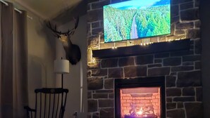 A stone fireplace with a TV mounted above it, a wooden table in front, and a chair to the left. - Just Like Home, brand new 2 bedroom rancher with full kitchen. (Mohnton)